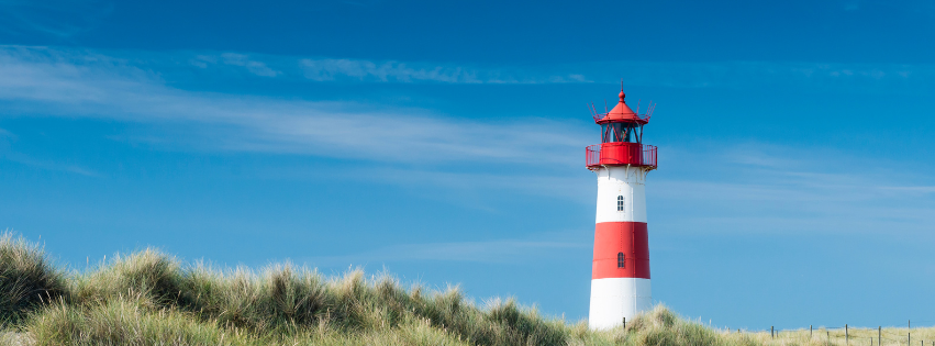 Roter und weißer Leuchtturm in Dünenlandschaft unter blauem Himmel als Symbol für Orientierung und Stabilität bei Burnout