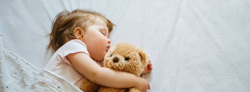 Kleines Kind schläft ruhig und entspannt mit einem Teddybären im Arm auf hellem Hintergrund