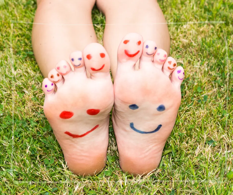 Zwei bloße Füße mit aufgemalten lächelnden Gesichtern liegen entspannt im Gras – Symbolbild für den Wohlfühlort
